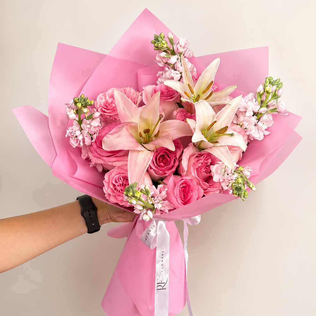A bouquet of pink roses, lilies, and small white flowers wrapped in pink paper delivered same-day in chicago 